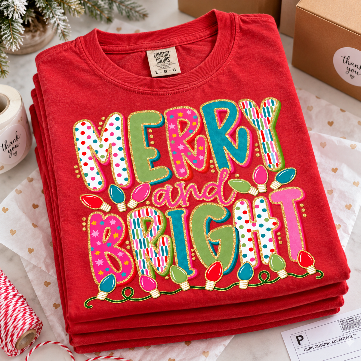 Red folded Comfort Colors Merry and Bright Christmas graphic tee with colorful patterned text and Christmas lightbulbs